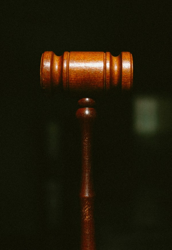 An upright wooden gavel in front of a dark background.