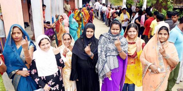 Several women outside a polling booth holding up their fingers with the marks of indelible ink.